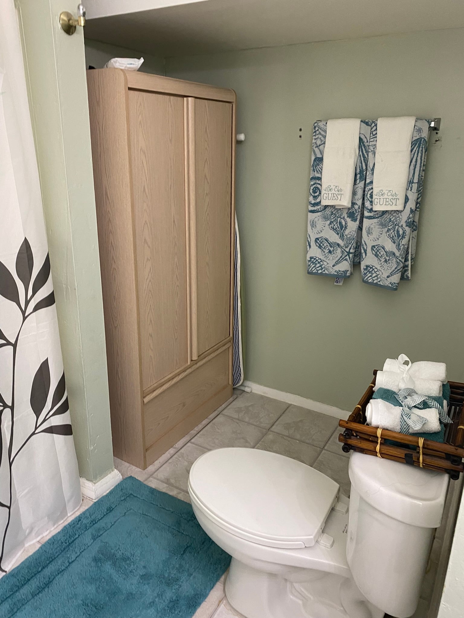 Shared bathroom with shower, toilet, storage cabinet, and towels